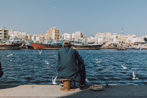 Serene view of the Dubai Creek with traditional dhow boats and a man enjoying the waterfront.
