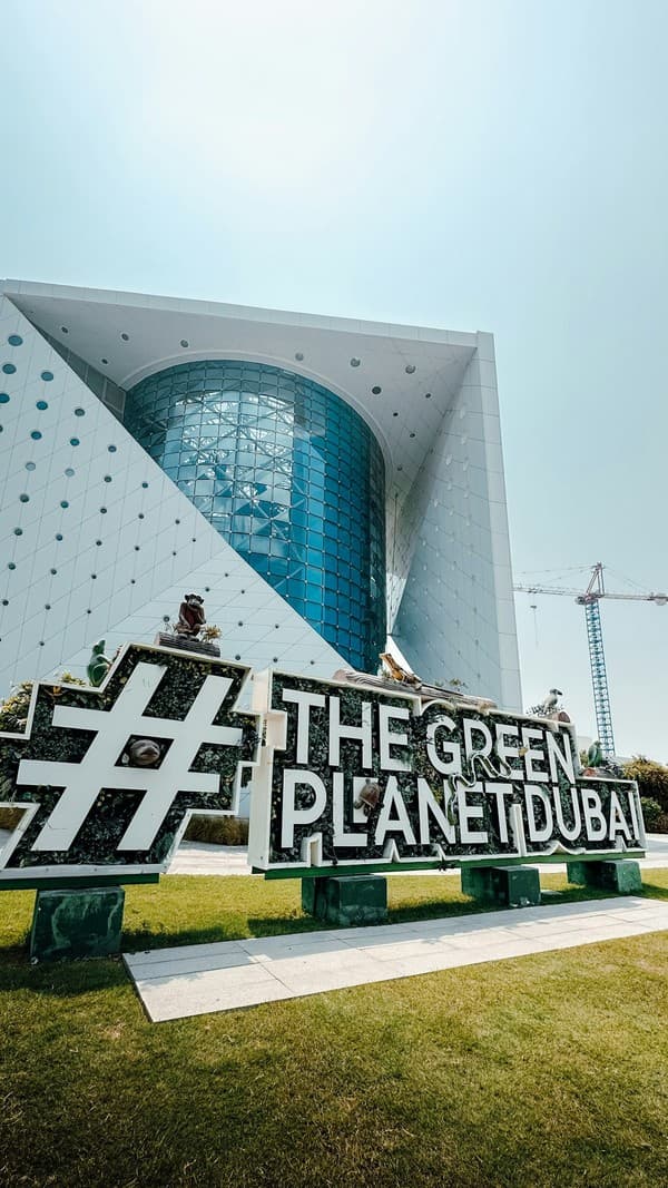 The green planet dubai sign is in front of a building.