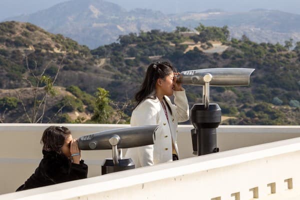 Two women enjoying a summer view through telescopes at an observatory terrace.
