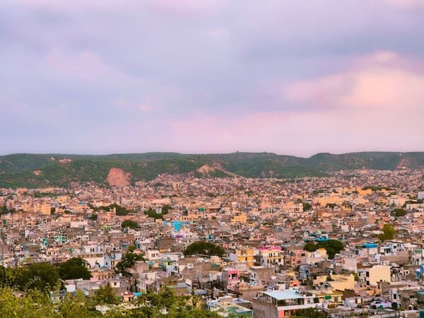 A panoramic view of Jaipur, Rajasthan during sunset, showcasing a blend of urban structures and natural landscape.