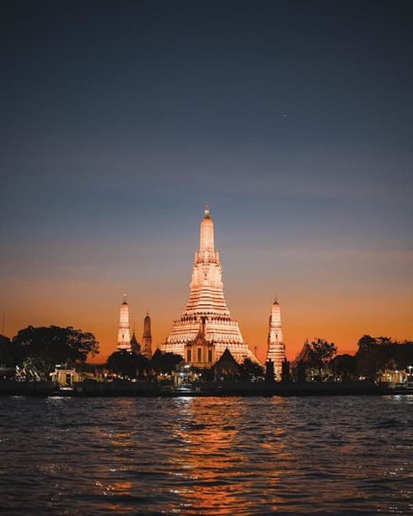 Beautiful view of Wat Arun temple illuminated during sunset along the Chao Phraya River in Bangkok, Thailand.