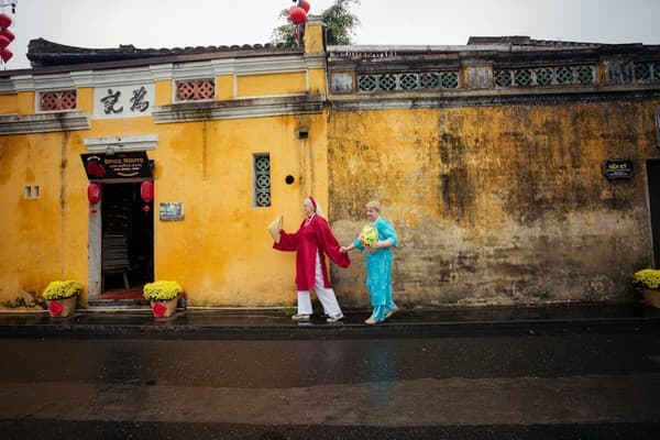 A couple in traditional attire walking in front of Hội An's historic yellow walls. A couple in traditional attire walking in front of Hội An's historic yellow walls.