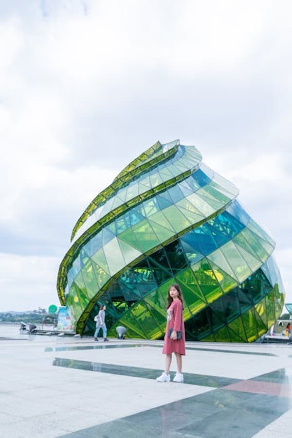 A young Asian woman poses in front of the iconic glass structure in Da Lat, Vietnam, on a sunny day.